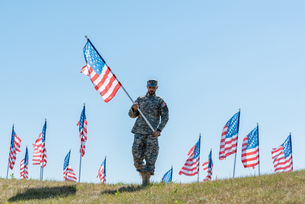 stock-photo-handsome-soldier-military-uniform-cap-holding-american-flag-while-standing