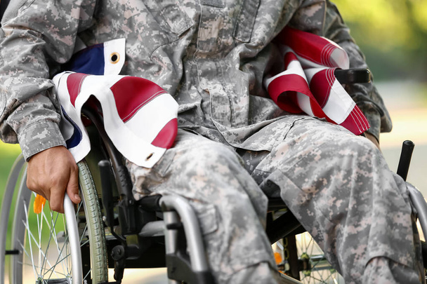 Young soldier in wheelchair with USA flag outdoors, closeup